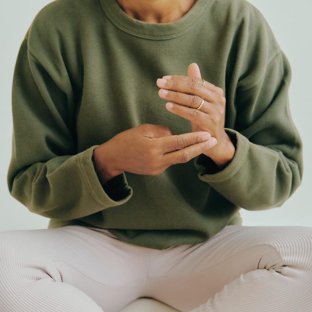 A photo of a woman seated cross-legged, feeling her pulse in her hand.